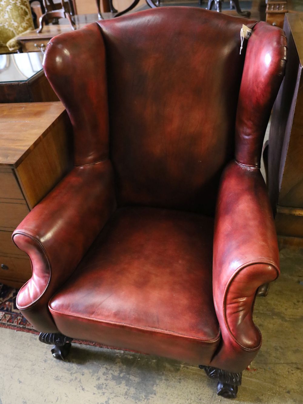 An early 20th century wing back armchair upholstered in burgundy leather on carved claw and ball feet, width 80cm, depth 82cm, height 1